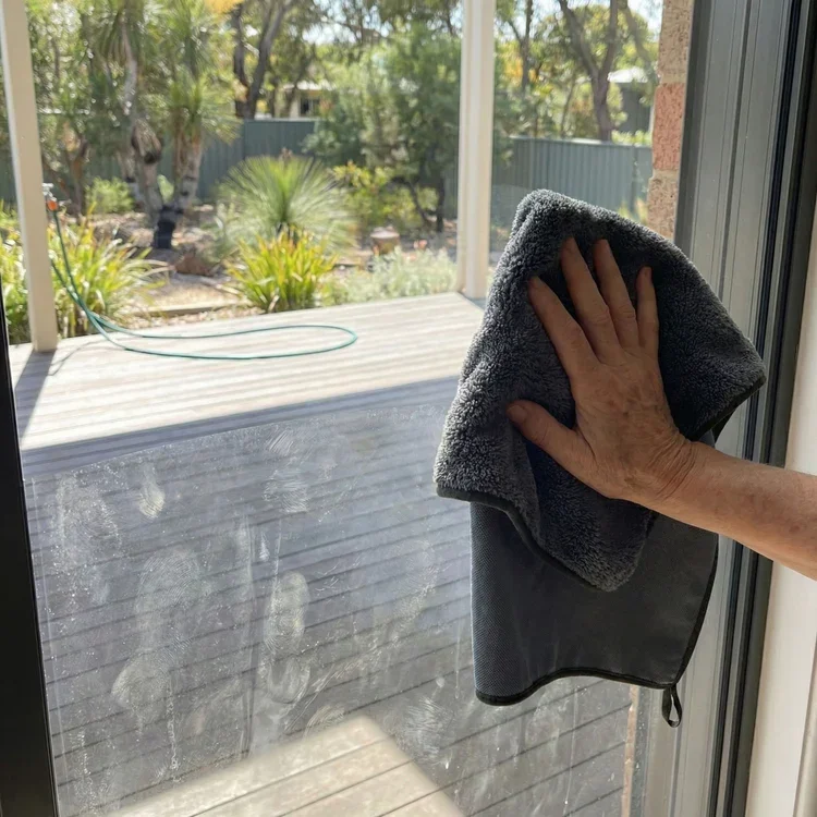 Cleaning a glass door with a dark grey cloth
